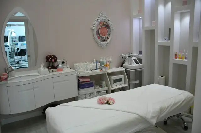 Una cabina di Malva: lettino bianco, specchio ovale e prodotti in ordine sulle mensole